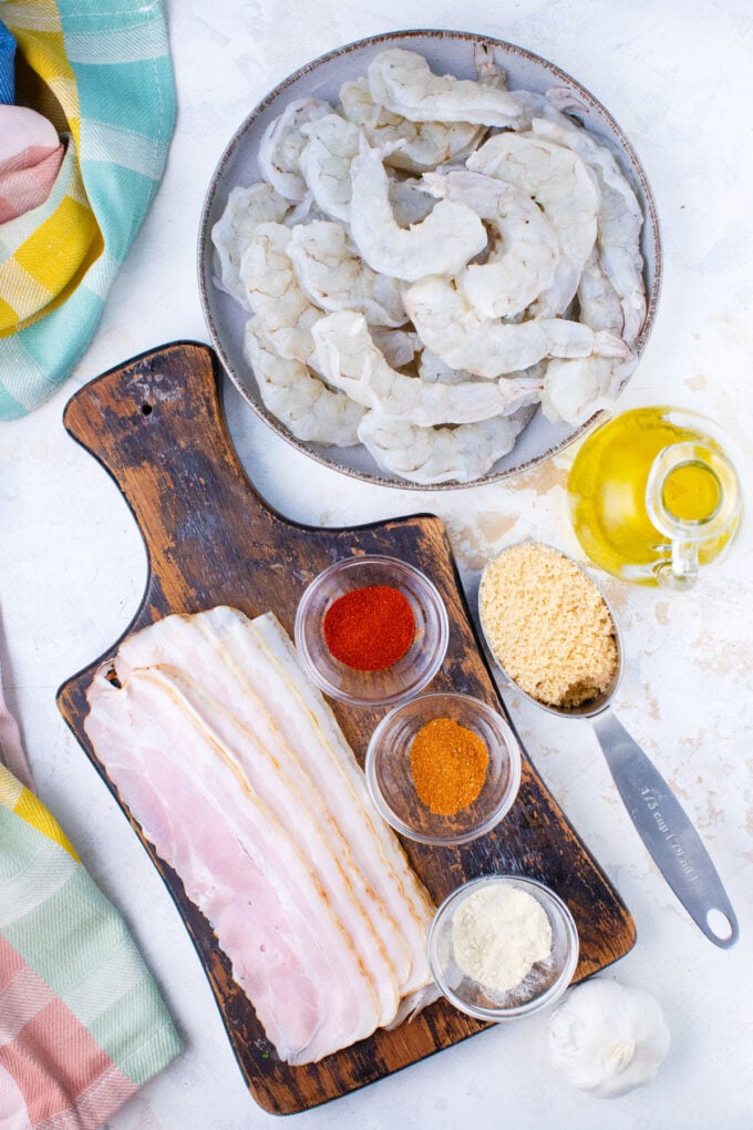 Overhead shot of bacon wrapped shrimp with brown sugar ingredients arranged on a white surface.