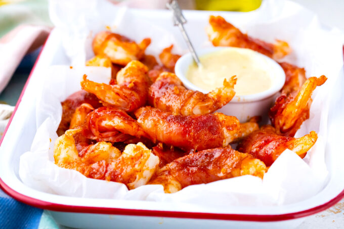 A tray of bacon wrapped shrimp with brown sugar with creamy sauce.