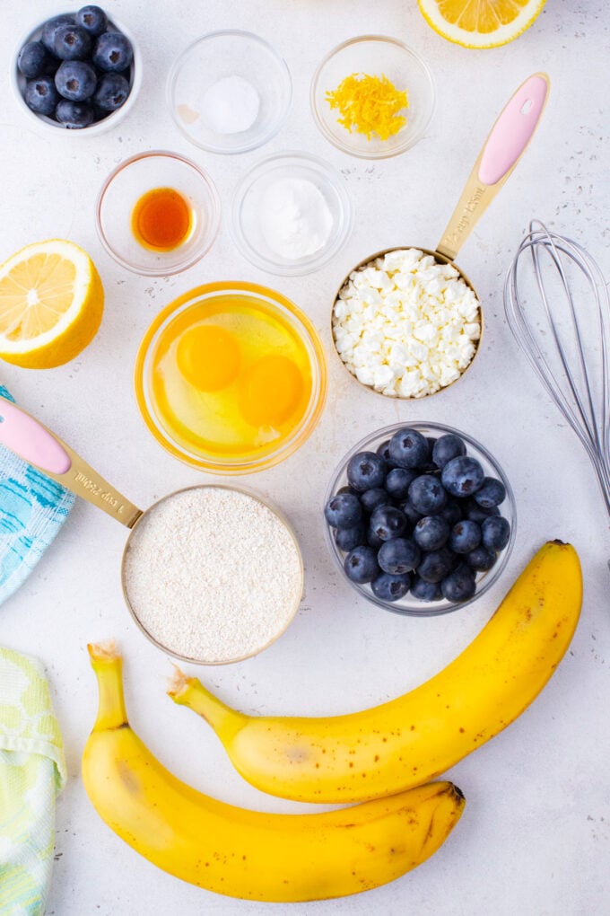 Overhead shot of blueberry gluten free cottage cheese banana waffles ingredients in bowls on a white surface.