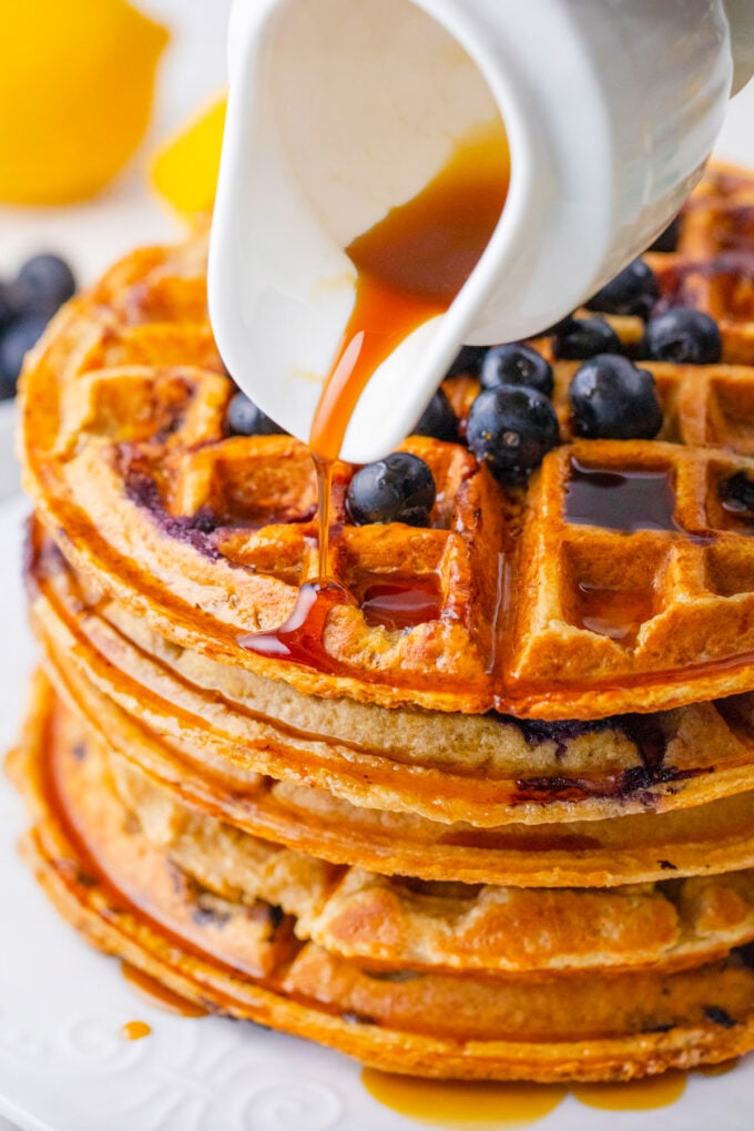 Pouring maple syrup over a stack of gluten free cottage cheese banana waffles.