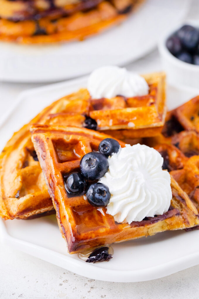 Blueberry gluten free cottage cheese banana waffles slices with fresh blueberries and whipped cream.