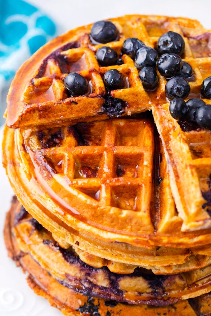 A stack of blueberry gluten free cottage cheese banana waffles slices with fresh blueberries and whipped cream.