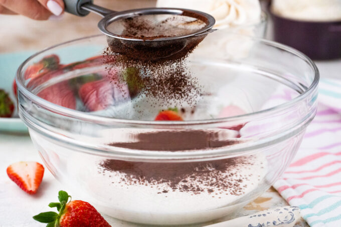 Sifting cocoa powder into a bowl with heavy cream.