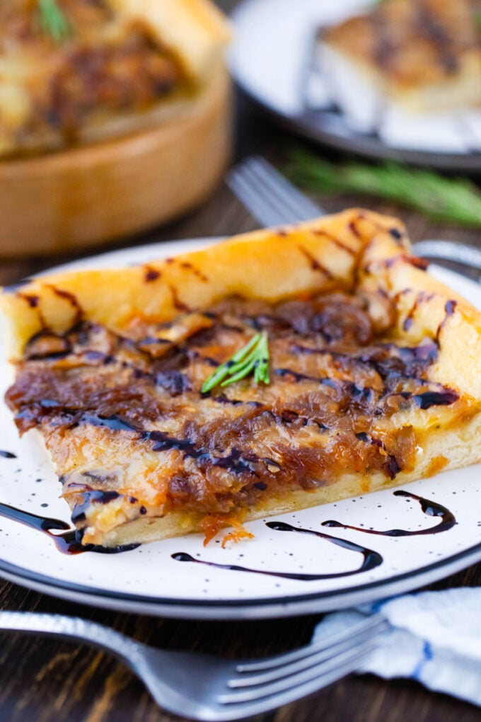 A slice caramelized onion tart served with a drizzle of balsamic reduction.
