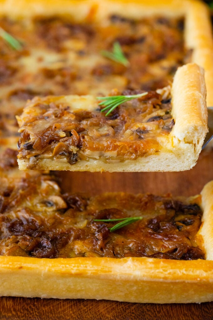 A slice of cheesy caramelized onion tart on a serving spatula.