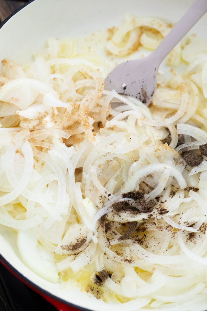 Cooking sliced onions with brown sugar, garlic, salt, and pepper in a skillet.