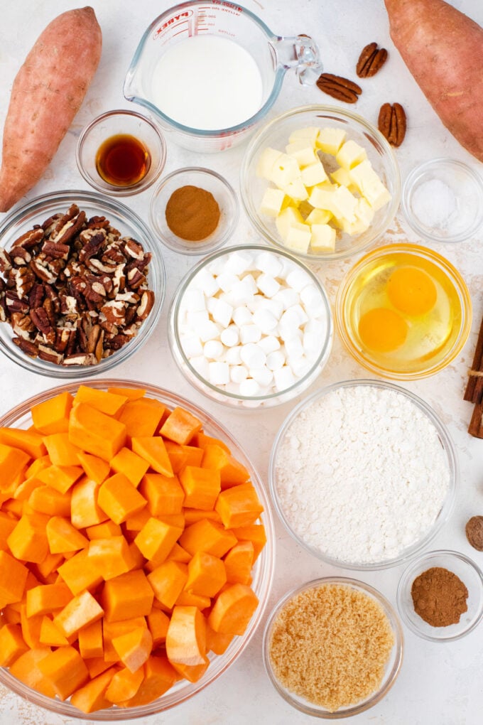Overhead shot of sweet potato casserole ingredients in bowls on a white surface.
