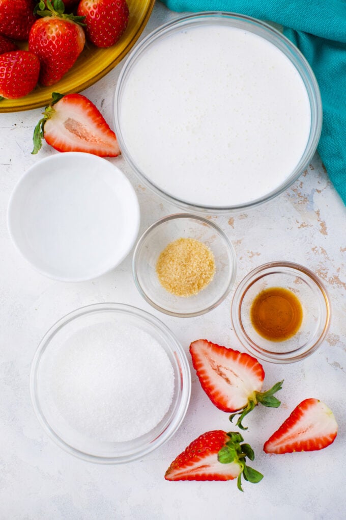 Overhead shot of stabilized whipped cream ingredients in bowls on a white surface.