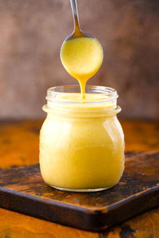 Honey mustard sauce dripping of a spoon into a jar.