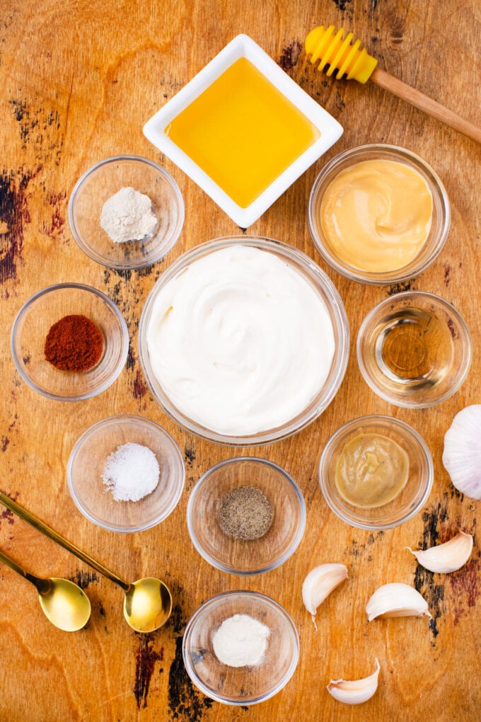 Overhead shot of honey mustard sauce ingredients in bowls on a wooden table.
