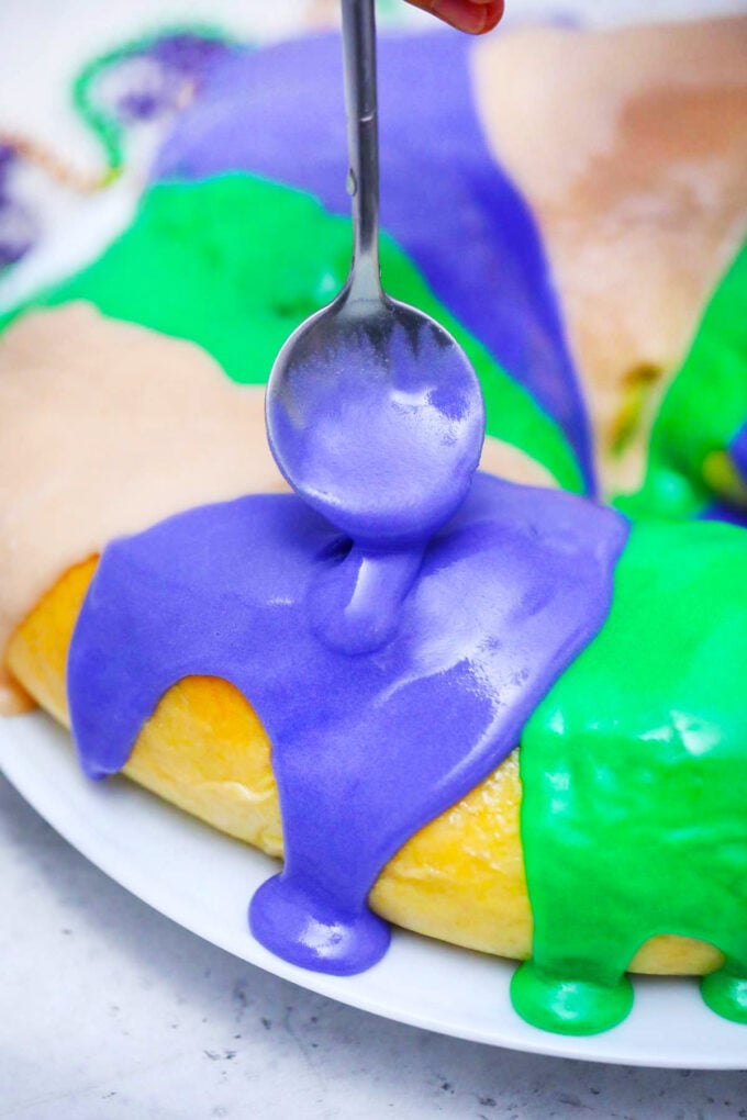 Adding purple icing over Mardi Gras King cake.