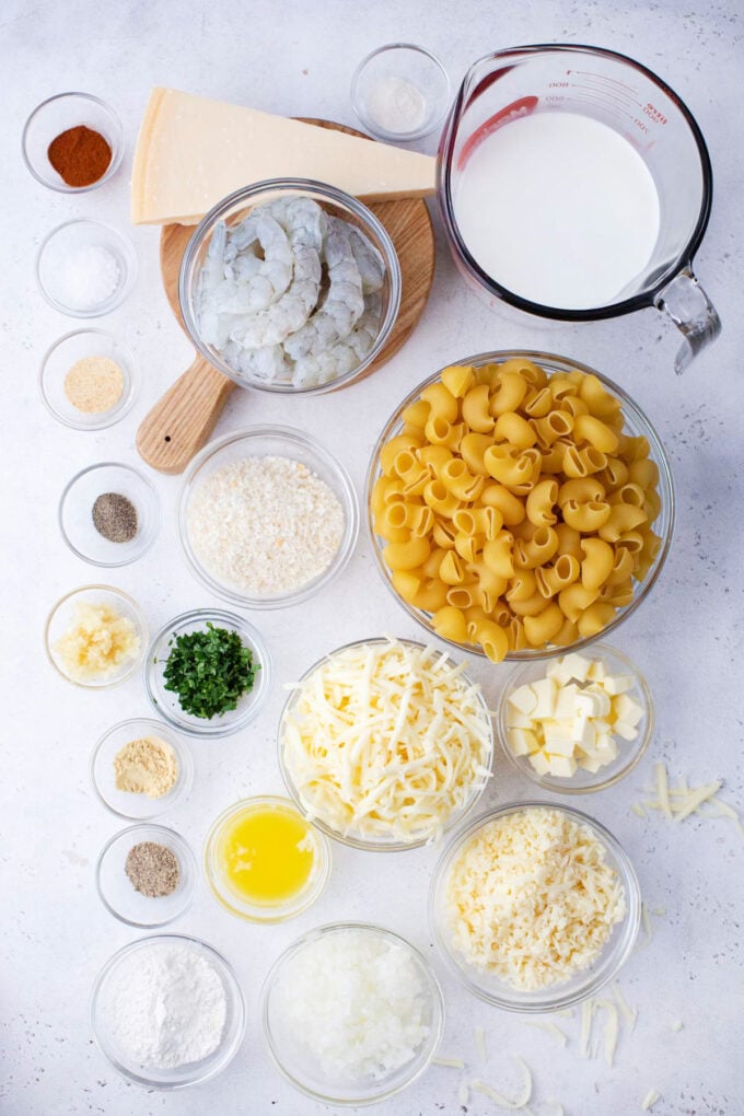 Overhead shot of four cheese shrimp mac and cheese ingredients in bowls on a white surface.