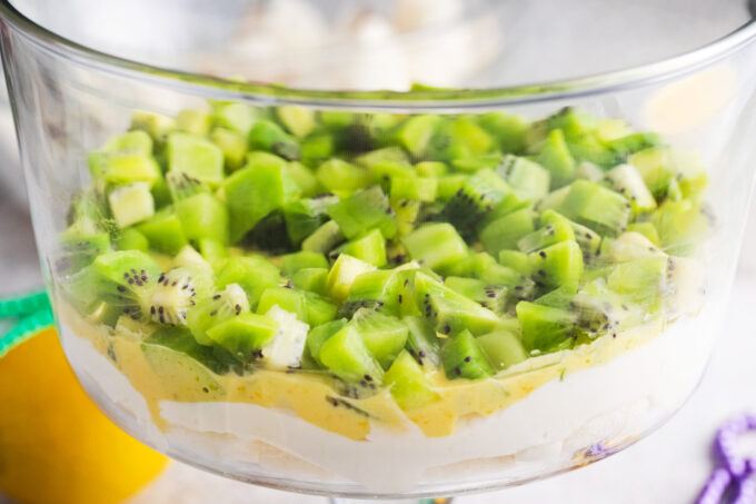 Layering cream cheese, lemon curd and kiwi in a bowl.