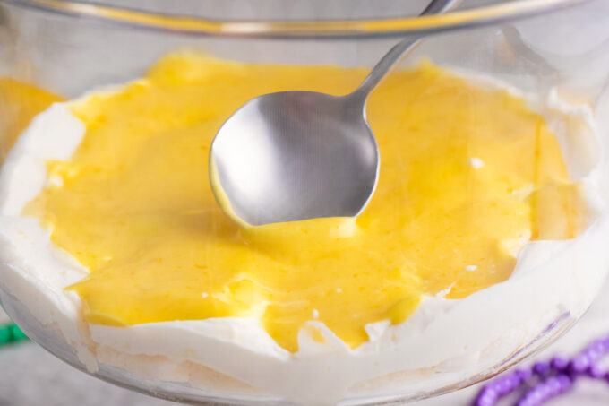 Spreading lemon curd over cream cheese layer in a trifle dish.