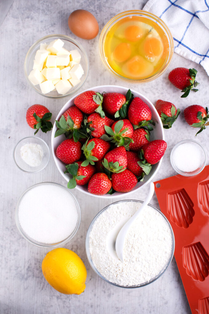 Overhead shot of strawberry madeleines ingredients in bowls on a white table.