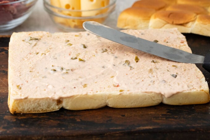 Spreading Russian dressing over Hawaiian rolls.