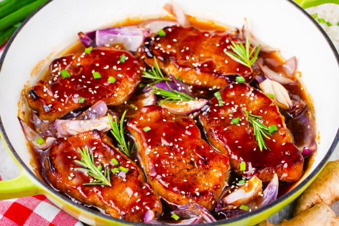 A pan of juicy General Tso pork chops with red onions and rosemary.