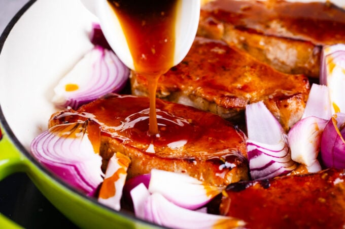 Adding general Tso sauce to a pan with seared pork chops and red onions.