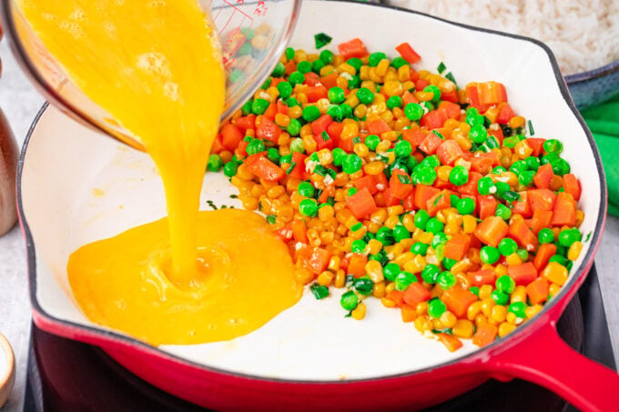 Pushing sauteed veggies to the side and adding beaten eggs to the pan.