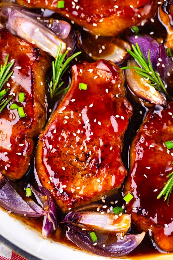 Close shot of sticky General Tso pork chops with red onions and sesame seeds.