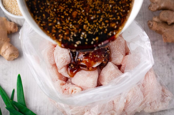 Adding honey sesame sauce to chicken pieces in a Ziploc bag.