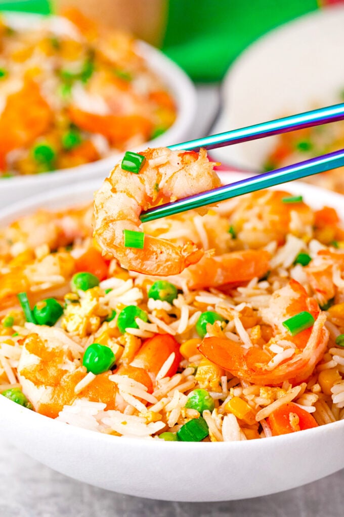 Holding a shrimp with a chopstick on top of a bowl of shrimp fried rice.