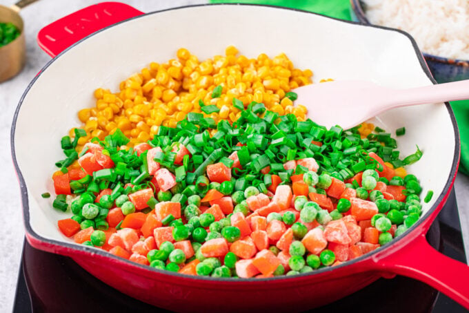 Sautéing corn, sweet peas, carrots, and green onions in a pan.