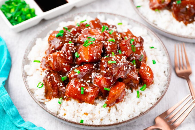 Slow cooker sesame chicken over rice, garnished with chopped green onions and sesame seeds.