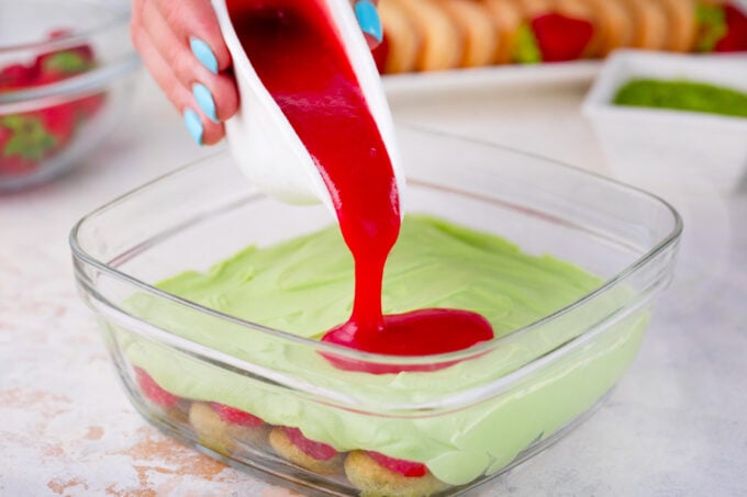 Layering matcha strawberry tiramisu in a glass container.